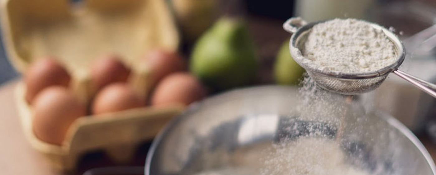 Sifting flour with eggs in the background