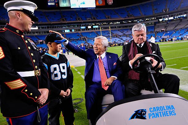 Owner Robert Kraft of the New England Patriots jokes with a young fan as owner Jerry Richardson of the Carolina Panthers signs an autograph before...