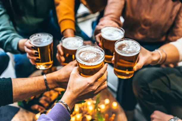 group of friends drinking and toasting glass of beer at brewery pub restaurant- happy multiracial people enjoying happy hour with pint sitting at bar table- youth food and beverage lifestyle concept - brewery stock pictures, royalty-free photos & images