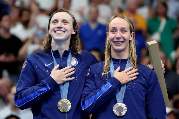 Gold Medalist Katie Ledecky and Bronze Medalist Paige Madden of Team United States sing their national anthem on the podium during the Swimming medal...