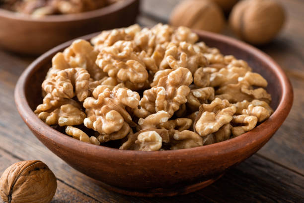 walnuts in brown bowl on wooden table - walnuts stock pictures, royalty-free photos & images