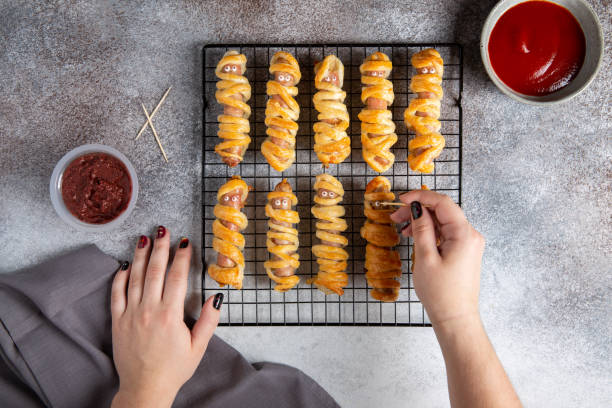 halloween mummy hot dogs. sausages with eyes wrapped in dough on cooling rack on concrete background. crazy funny halloween food. food preparation. top view, flat lay. - mummy hot dog stock pictures, royalty-free photos & images