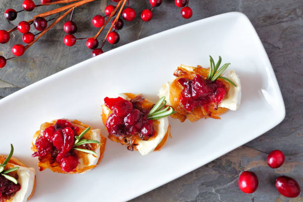 crostini appetizers with cranberries, brie and caramelized onions, above on a white plate - cranberry brie bites stock pictures, royalty-free photos & images