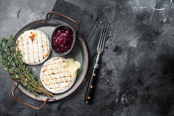 baked camembert cheese on a steel tray with cranberry sauce and thyme. black background. top view. copy space. - cranberry brie stock pictures, royalty-free photos & images