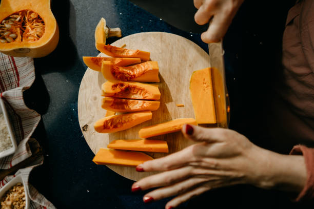 caucasian woman slicing a butternut squash on a wooden cutting board. - butternut squash stock pictures, royalty-free photos & images