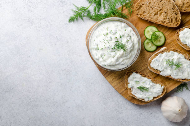 homemade greek tzatziki sauce in a glass bowl with ingredients and sliced bread on a wooden board and light stone background. cucumber, lemon, dill. top view, horizontal image, copy space - dill dip stock pictures, royalty-free photos & images