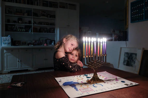 two sisters standing together looking at hanukkah menorah fully lit - hanukkah stock pictures, royalty-free photos & images