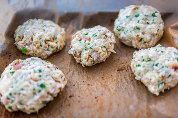 macro closeup of raw uncooked crab crabmeat fish cakes on parchment paper of baking oven tray in kitchen with herns - making crab cakes stock pictures, royalty-free photos & images