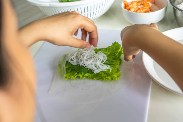 woman wrapping vietnamese rice noodle shrimp roll- goi cuon - making summer rolls stock pictures, royalty-free photos & images