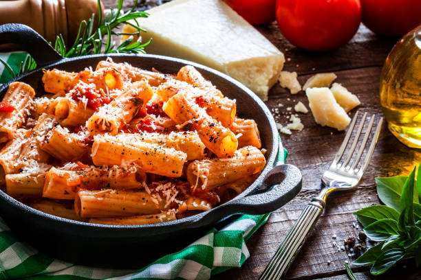 pasta in a cast iron pan shot on rustic wooden table - rigatoni baked pasta stock pictures, royalty-free photos & images